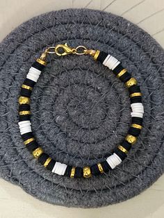 a black and white bracelet with gold beads on a gray surface next to a pair of scissors