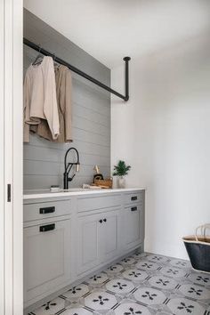 a kitchen with white cabinets and gray tile flooring is pictured in this image, there are clothes hanging on the rack next to the sink