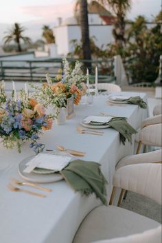 a long table is set up with flowers and place settings for an outdoor wedding reception