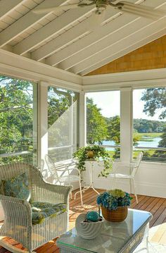 a screened porch with wicker furniture and large windows looking out onto the water in the distance