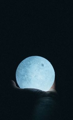 a hand holding a lit up moon in the dark