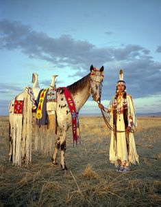 a native american man standing next to a horse in the middle of an open field