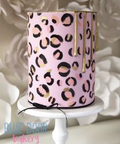 a pink leopard print cake with gold trimmings on a white pedestal against a floral background