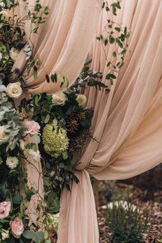 a wedding arch with flowers and greenery on the top is covered by draping