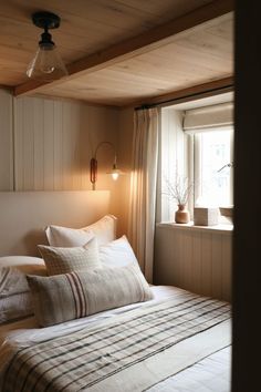 a bed sitting under a window next to a wooden wall mounted light above it's headboard