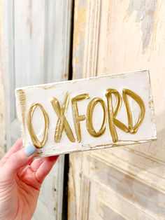 a person holding up a sign with the word oxford written in gold paint on it