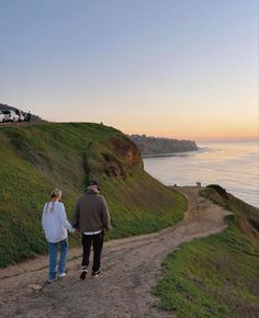 a man and woman walking down a dirt road next to the ocean