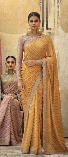 two women in sari standing next to each other with one woman sitting on the ground