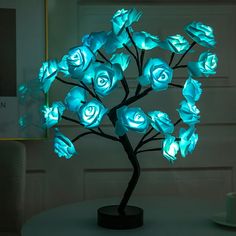 there is a small tree that has blue roses on it and some lights in the shape of flowers