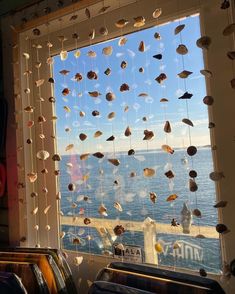 a window with shells hanging from it's side and the ocean in the background