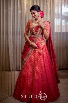 a woman in a red and gold lehenga standing next to a curtain with her hands on her face