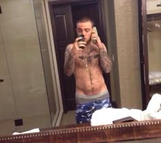 a shirtless man is taking a selfie in front of the mirror with his cell phone