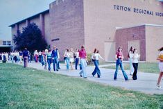 a group of people walking down a sidewalk in front of a brick building with the words triton regional high school on it