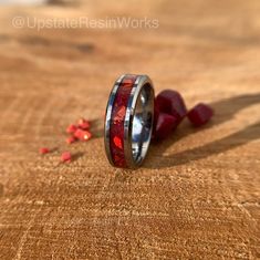 a wedding band with red and black inlays sits on a piece of wood