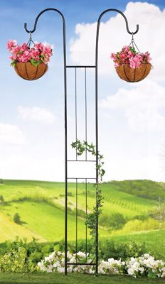 two hanging baskets filled with flowers on top of a metal pole in the middle of a lush green field