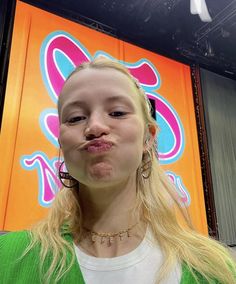 a woman with long blonde hair and piercings making a face while standing in front of a sign