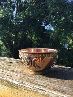 a brown bowl sitting on top of a wooden table in front of some green trees