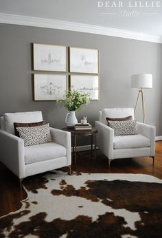 a living room with two white chairs and pictures on the wall