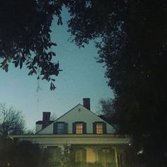 a large white house sitting in the middle of a tree filled forest at night with its lights on