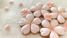 decorated cookies with pink icing and flowers on a white tablecloth, ready to be eaten