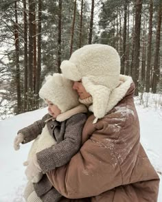 a woman holding a child in her arms while walking through the snow covered woods on a cold day