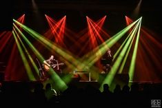 three people are on stage with green and red lights shining from their hands in front of them