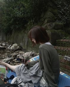 a woman sitting on top of a blue blanket next to a river