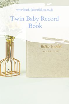 the twin baby record book is next to a vase with flowers in it and an empty box