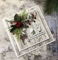 a christmas card with deer, holly and berries on the front is sitting next to a pine tree