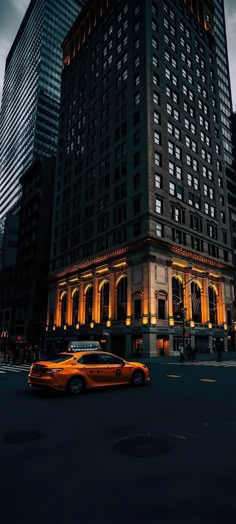 a yellow taxi driving past a tall building in the city at night with lights on