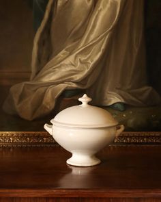 a large white bowl sitting on top of a wooden table next to a painting in a frame