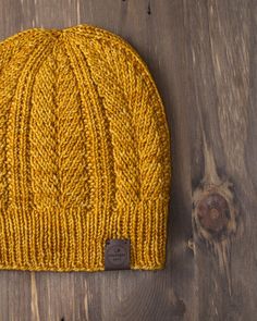 a yellow knitted beanie sitting on top of a wooden floor next to a piece of wood