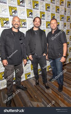 three men posing for the camera in front of a wall with comic characters on it