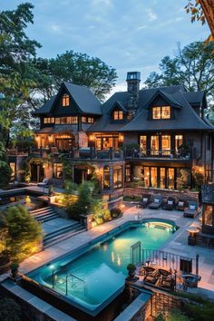 an outdoor swimming pool surrounded by trees and lights in front of a large house at dusk