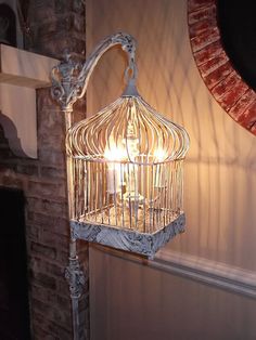 a birdcage hanging from the side of a brick wall next to a candle