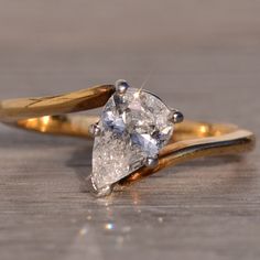 an engagement ring with two pear shaped diamonds on it, sitting on a wooden surface