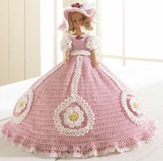 a crocheted doll in a pink dress and hat on a white tablecloth