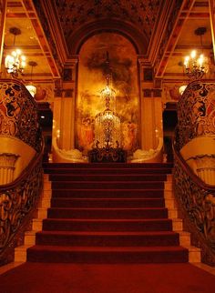 an ornate staircase with chandelier and paintings on the walls