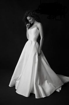 a woman in a white dress is posing for a black and white photo with her hand on her face