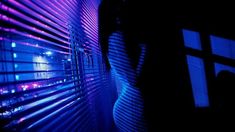 the silhouette of a person standing in front of a window covered in purple and blue lights