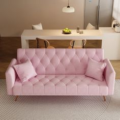 a pink couch sitting on top of a rug next to a white table and chairs