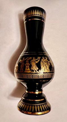 a black vase with gold designs on the top and bottom, sitting against a white wall