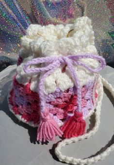 a crocheted bag with tassels on the front and side, sitting on top of a table