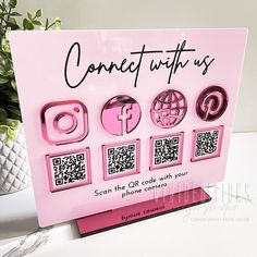 a pink greeting card with qr code and icons on it, sitting next to a potted plant