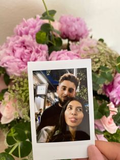 a person holding up a polaroid photo with flowers in the back ground behind them