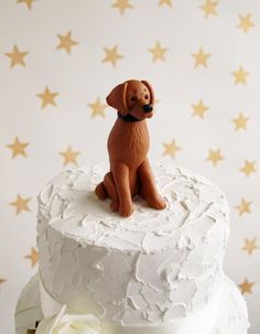 a white cake with a brown dog figurine on top and gold stars in the background