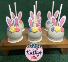 four cake pops with bunny ears and flowers in them on a wooden table next to a sign that says kaby's