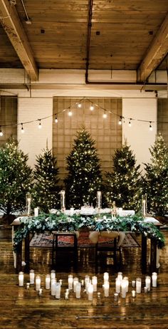 a long table with candles and christmas trees in the background is surrounded by greenery