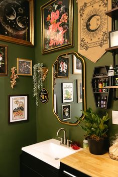 a bathroom with green walls and lots of pictures on the wall, including an oval mirror