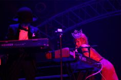 a woman wearing a crown sitting in front of a keyboard with a man standing behind her